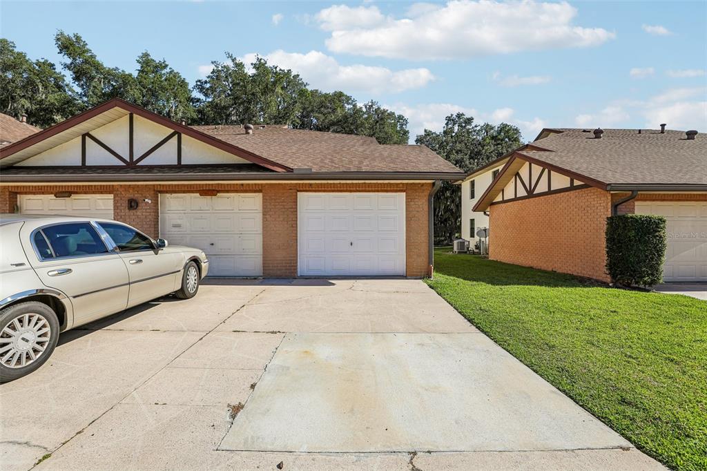 A view of two attached brick houses with white garage doors and a shared driveway — 100 E OAK TERRACE DRIVE UNIT D2, LEESBURG, FL