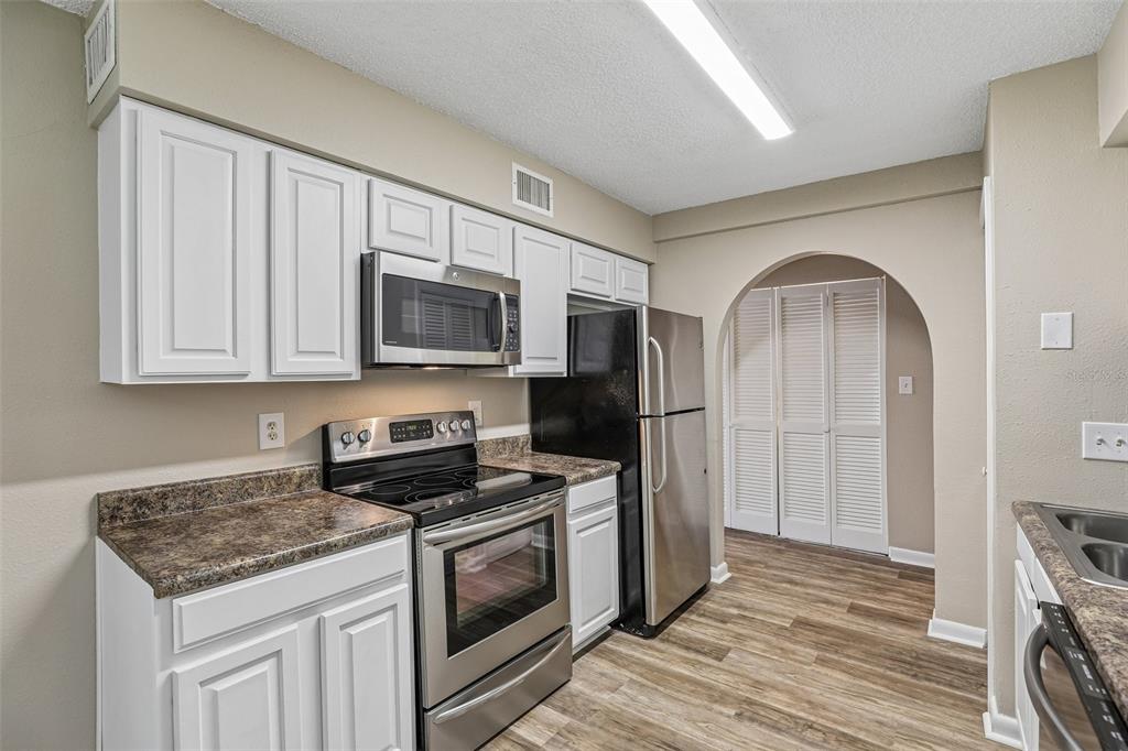 A kitchen features white cabinets, stainless steel appliances, dark countertops, and an arched doorway — 100 E OAK TERRACE DRIVE UNIT D2, LEESBURG, FL
