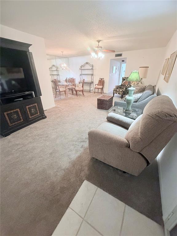 A living room with beige carpet, a large black entertainment center, and a dining area — 5301 LAKEFRONT BOULEVARD UNIT C, DELRAY BEACH, FL