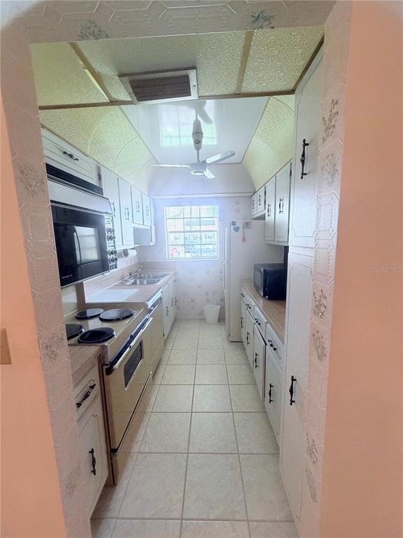 A galley kitchen features white cabinets, a beige range, a ceiling fan, and tiled flooring — 5301 LAKEFRONT BOULEVARD UNIT C, DELRAY BEACH, FL