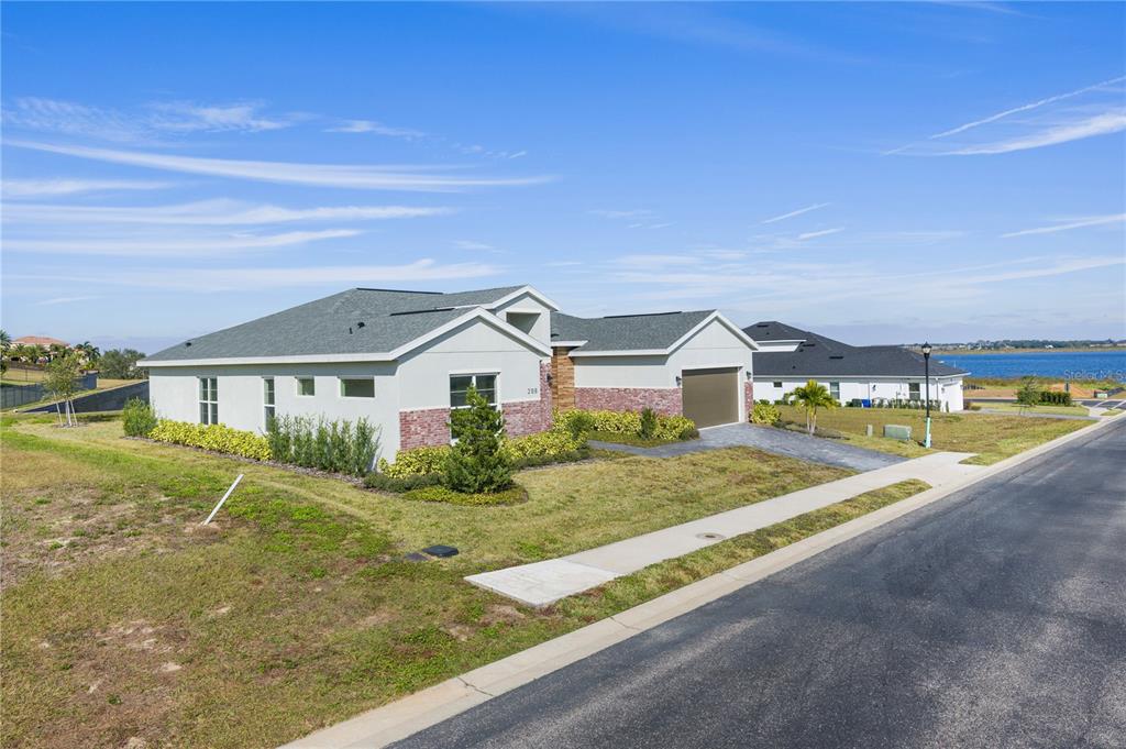 A modern single-story house with a brick facade and attached garage sits near a lake — 208 SNOWY ORCHID WAY, LAKE ALFRED, FL