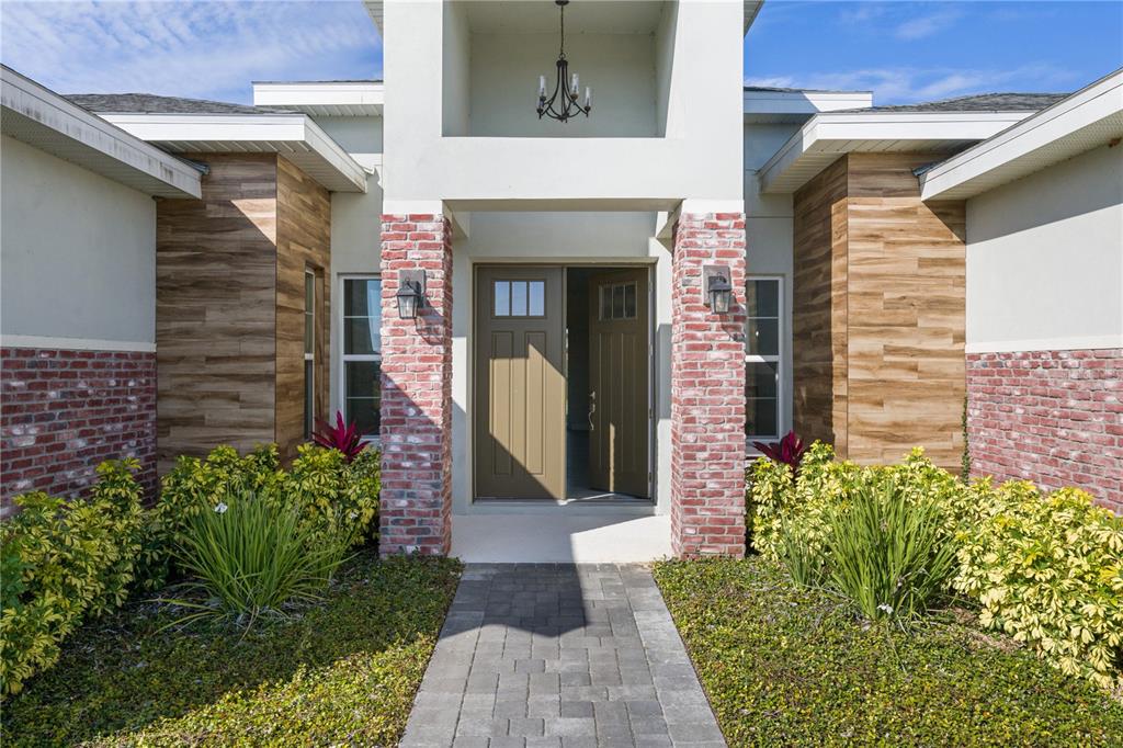 The front entrance of a house features a brick-accented porch, wood-look siding, and a walkway — 208 SNOWY ORCHID WAY, LAKE ALFRED, FL