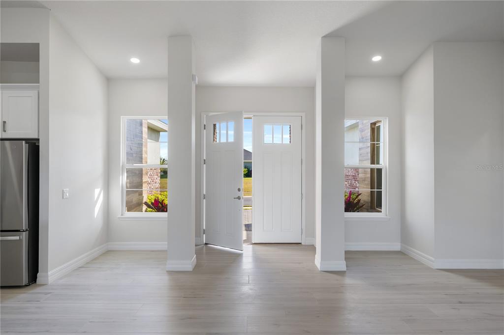 A bright entryway features light wood-look flooring, two white pillars, and a double front door — 208 SNOWY ORCHID WAY, LAKE ALFRED, FL