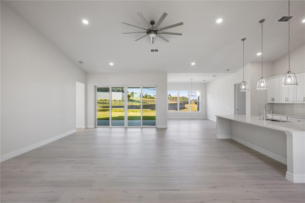 An open-concept living area features light wood floors, a large ceiling fan, and a kitchen — 208 SNOWY ORCHID WAY, LAKE ALFRED, FL