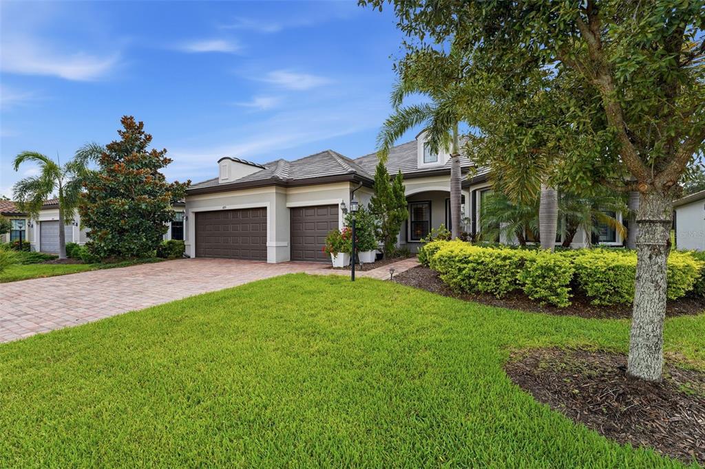 A single-story house with a brick driveway, two-car garage, and manicured landscaping under a blue sky — 6839 CHESTER TRAIL, BRADENTON, FL