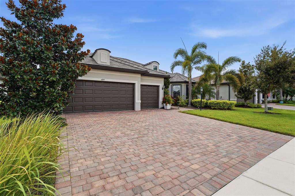 A single-story house features a brick paver driveway, a three-car garage, and palm trees — 6839 CHESTER TRAIL, BRADENTON, FL