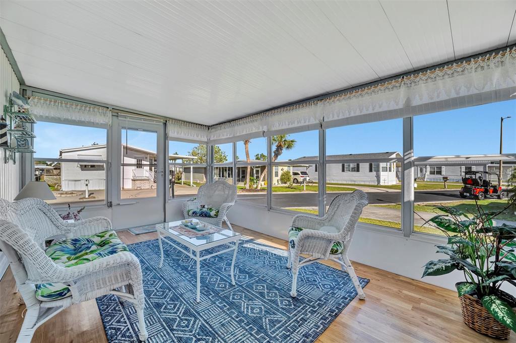 A sunroom features white wicker furniture, a blue patterned rug, and large windows overlooking neighborhood homes — 128 E SAINT JOHNS WAY, APOLLO BEACH, FL