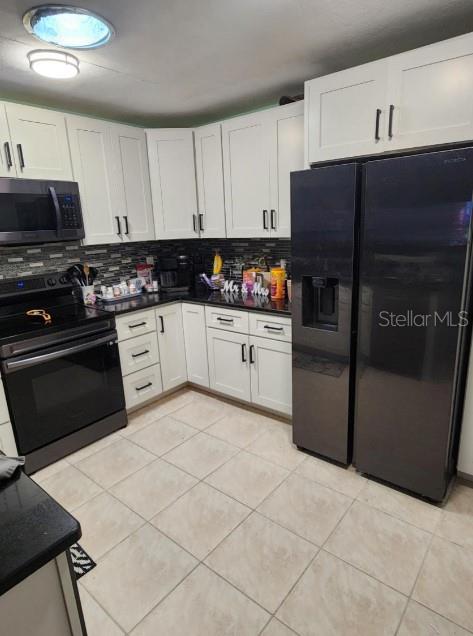 A kitchen features white cabinets, black appliances, and light-colored tile flooring — 5573 FOXLAKE DRIVE, NORTH FORT MYERS, FL