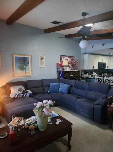 A large blue sectional sofa sits in a living room with a wood-beamed ceiling — 5573 FOXLAKE DRIVE, NORTH FORT MYERS, FL