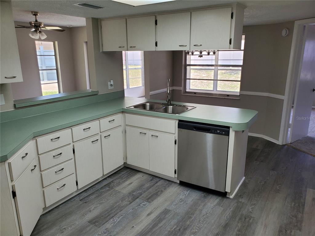 A kitchen features white cabinets, green laminate countertops, a stainless steel dishwasher, and wood-look flooring — 3936 SAILMAKER LANE, HOLIDAY, FL