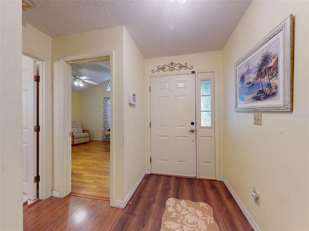 An entryway features wood-look flooring, a white front door with a sidelight, and wall art — 686 MIDDLEBURY LOOP, NEW SMYRNA BEACH, FL