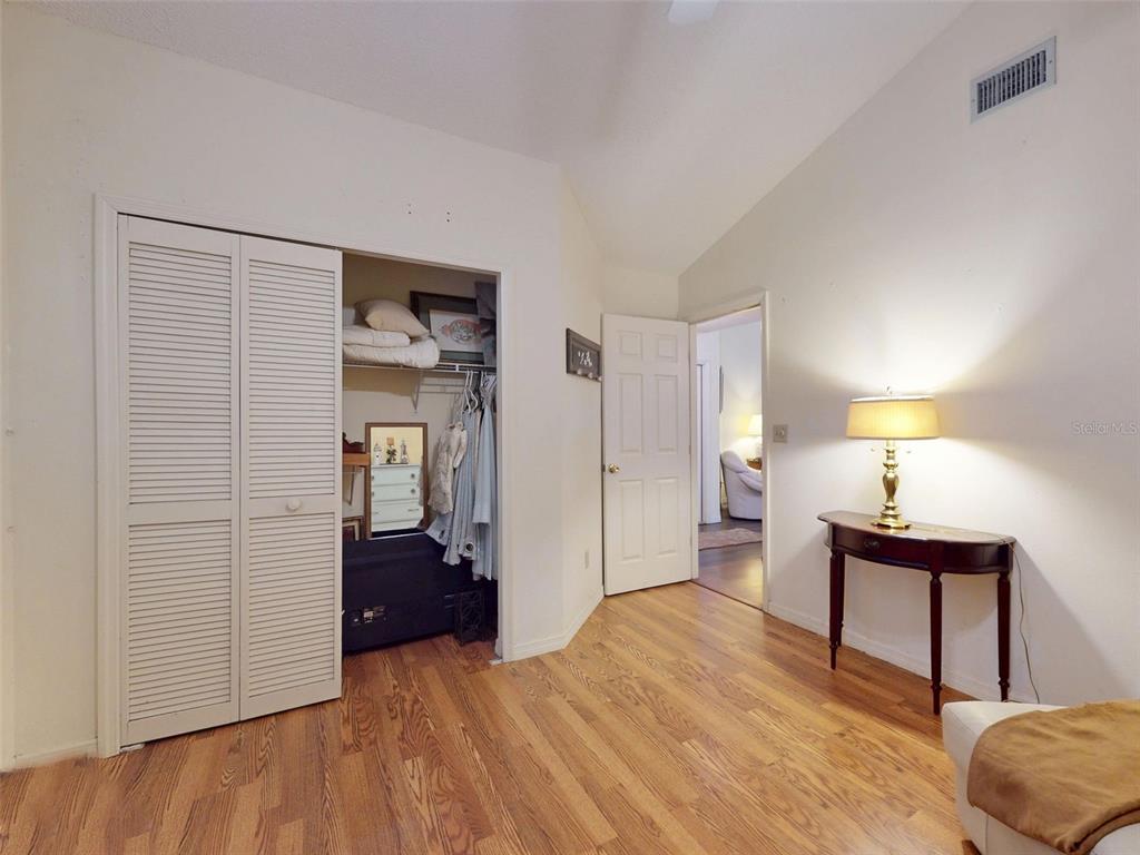 A bedroom features hardwood floors, a louvered closet, a console table with a lamp, and vaulted ceilings — 686 MIDDLEBURY LOOP, NEW SMYRNA BEACH, FL