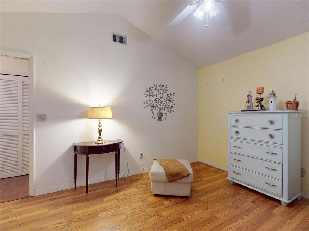 A room with hardwood floors, a vaulted ceiling, a dresser, a small table, and an ottoman — 686 MIDDLEBURY LOOP, NEW SMYRNA BEACH, FL