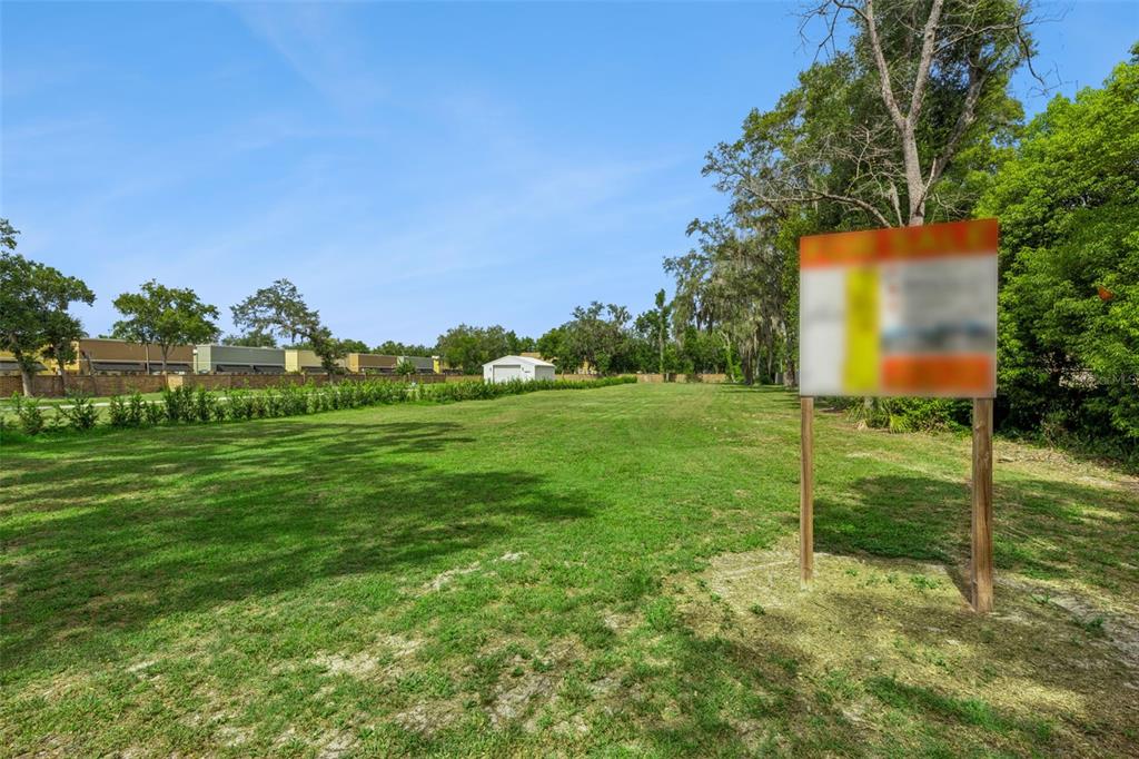 A grassy, vacant lot features a for-sale sign in the foreground and trees in the background — 136 N 9TH STREET, LAKE MARY, FL