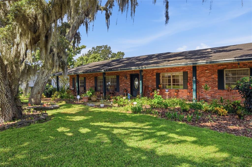 A single-story brick house with a covered porch, large oak tree, and landscaped front yard — 4211 FOREST HILLS DRIVE, LAKELAND, FL