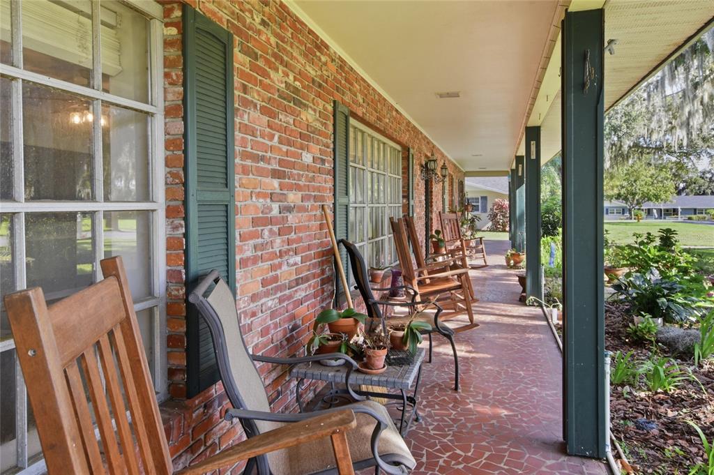 A long brick porch features rocking chairs, potted plants, and a tiled floor — 4211 FOREST HILLS DRIVE, LAKELAND, FL
