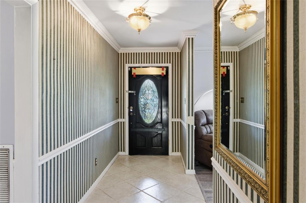 A foyer features striped wallpaper, a black front door with a glass insert, and tile flooring — 4211 FOREST HILLS DRIVE, LAKELAND, FL
