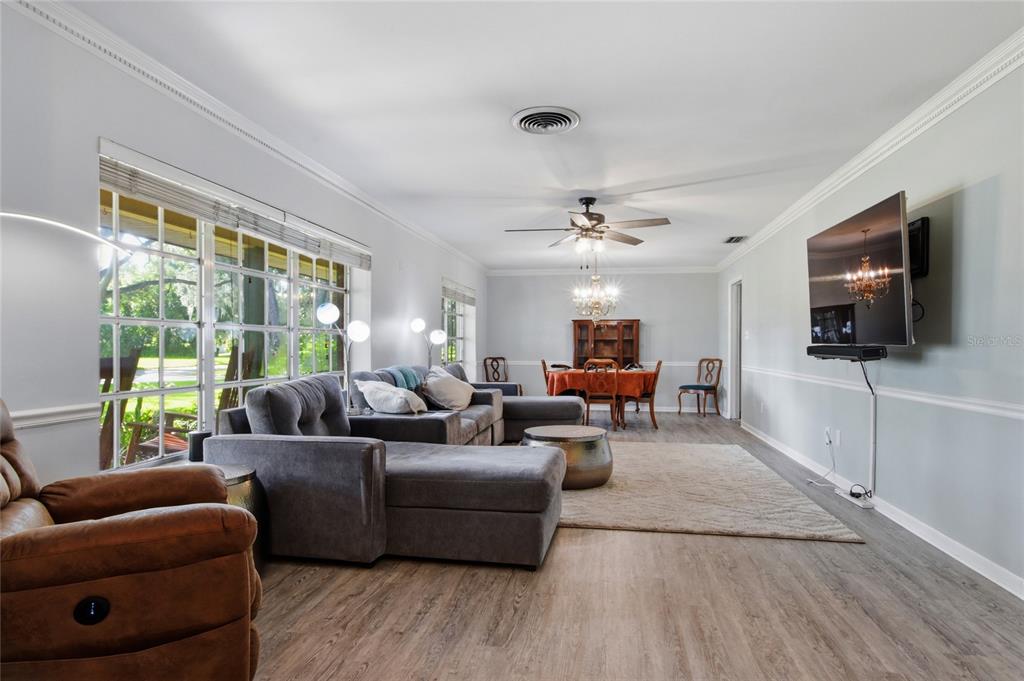 A living room with gray flooring, a sectional sofa, a dining area, and a wall-mounted television — 4211 FOREST HILLS DRIVE, LAKELAND, FL