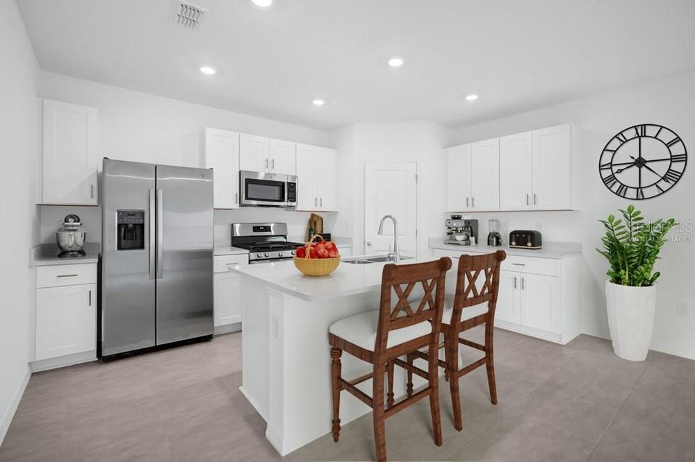 A modern kitchen features white cabinetry, stainless steel appliances, a center island, and tile flooring — 13835 SHELLMORE AVENUE, PALMETTO, FL