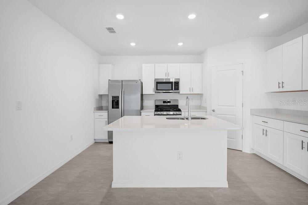 A modern kitchen features white cabinets, stainless steel appliances, and a central island with countertops — 13835 SHELLMORE AVENUE, PALMETTO, FL