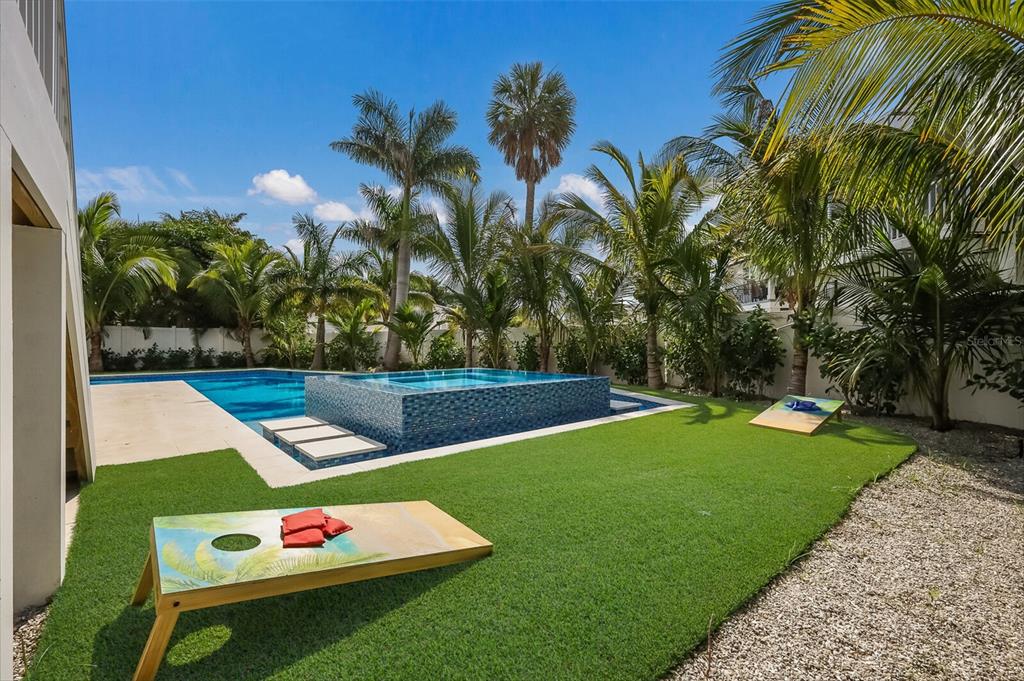 A backyard features a swimming pool with a raised spa, artificial turf, and cornhole boards — 227 S HARBOR DRIVE, HOLMES BEACH, FL