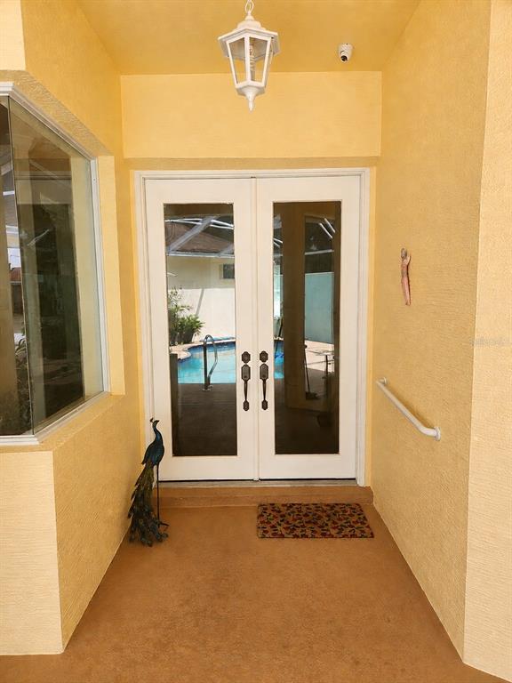 A covered entryway features yellow stucco walls, double glass doors, and a view of a pool — 7517 JOMEL DRIVE, WEEKI WACHEE, FL