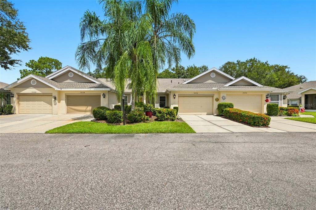A street-level view of a single-story duplex with two garages and a central palm tree — 2472 NANTUCKET HARBOR LOOP, SUN CITY CENTER, FL