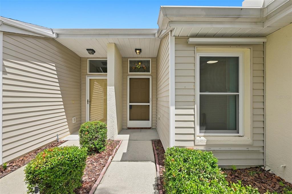 A beige house exterior features a front entrance with a screen door and two bushes — 2472 NANTUCKET HARBOR LOOP, SUN CITY CENTER, FL