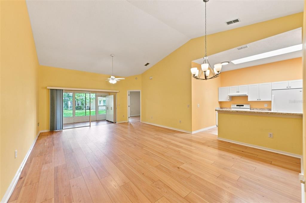 An open-concept living and dining area with yellow walls, wood flooring, and a white kitchen — 2472 NANTUCKET HARBOR LOOP, SUN CITY CENTER, FL