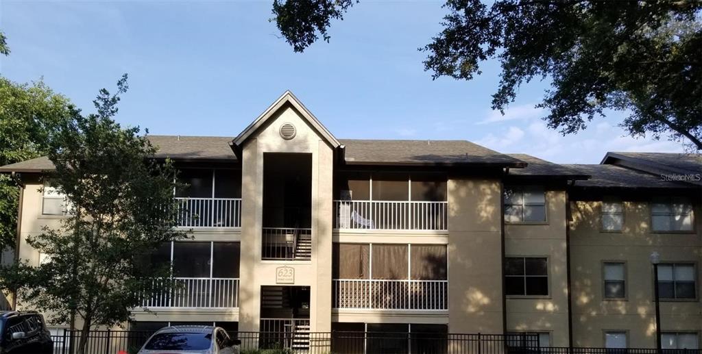 A three-story apartment building exterior features screened balconies and a parking lot in front — 623 DORY LANE UNIT 306, ALTAMONTE SPRINGS, FL