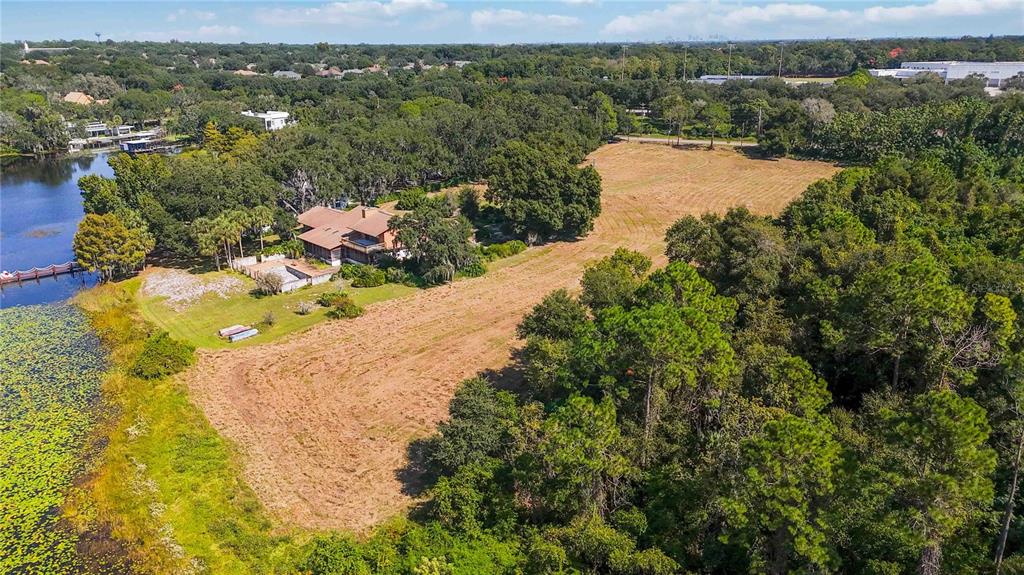 An aerial view shows a house with a pool situated beside a lake and field — 4226 DOWNEAST LANE, WINDERMERE, FL