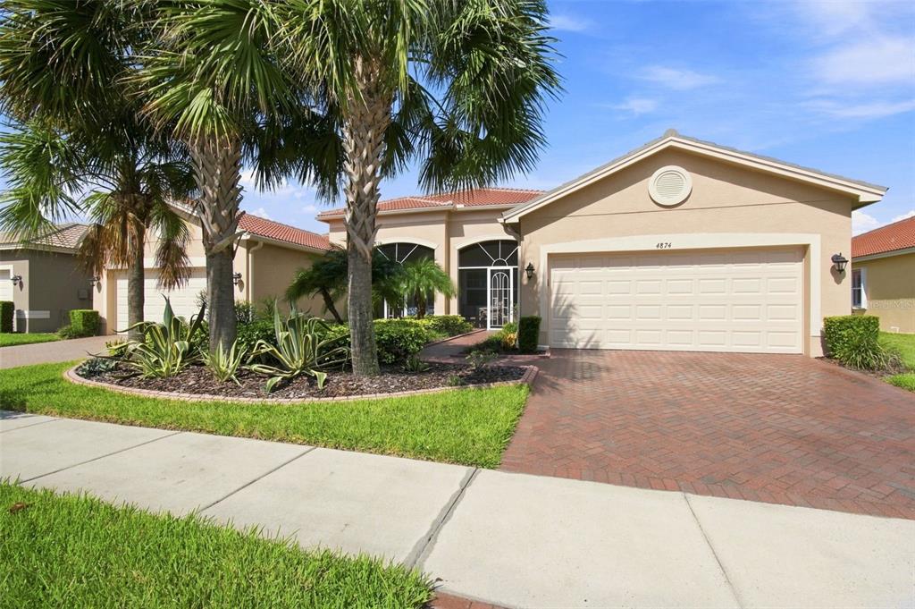 A single-story house with a tan stucco exterior, a brick driveway, and palm trees — 4874 MARBLE SPRINGS CIRCLE, WIMAUMA, FL