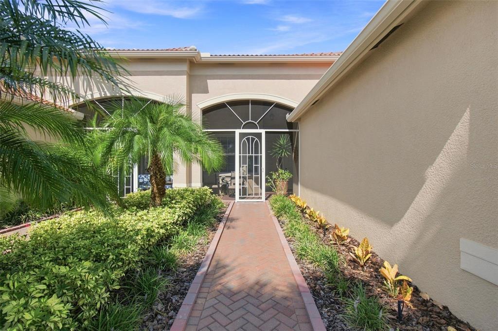 A brick walkway leads to a screened entryway of a beige house with landscaping — 4874 MARBLE SPRINGS CIRCLE, WIMAUMA, FL