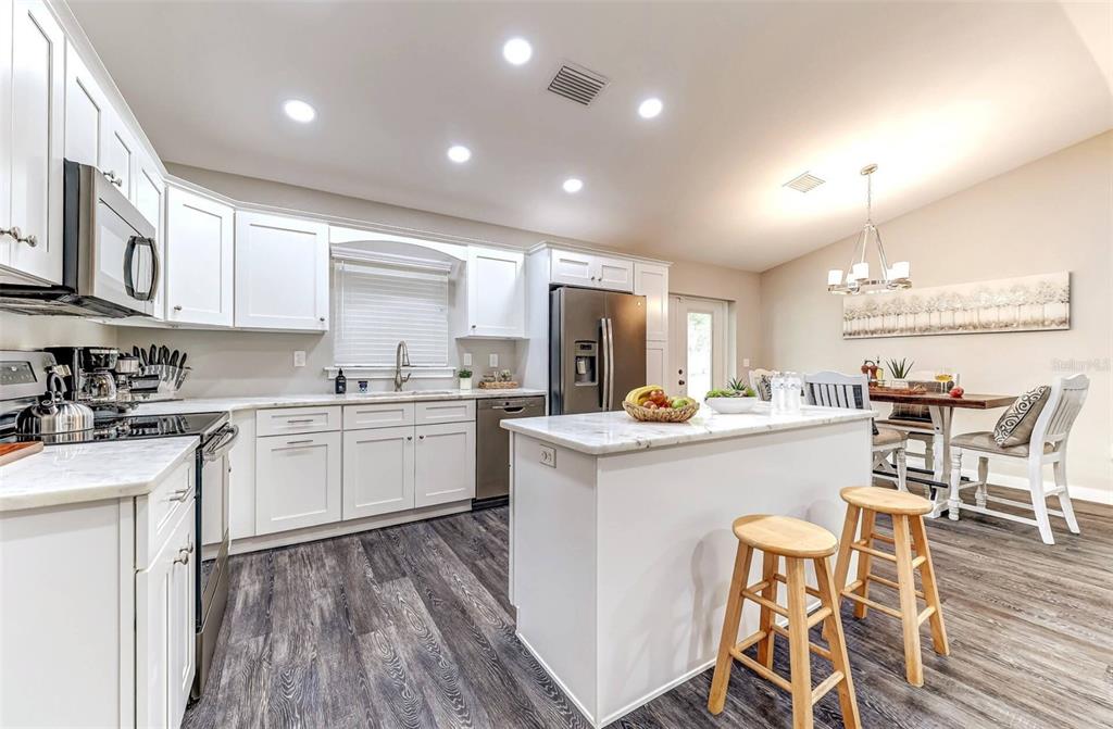 A white kitchen features a marble-topped island, stainless steel appliances, and dark wood-look flooring — 220 KITE AVENUE, SEBRING, FL