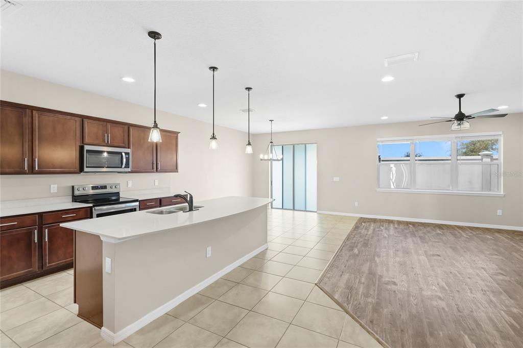 A kitchen with dark wood cabinets, a white island, and tile flooring next to a room — 6574 KENAVA LOOP, PALMETTO, FL