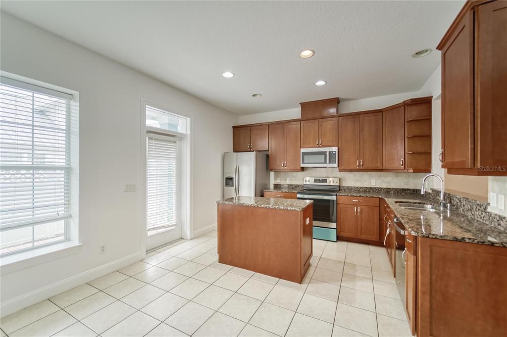 A kitchen features wood cabinets, granite countertops, a center island, and white tile flooring — 5405 CAFREY PLACE, APOLLO BEACH, FL