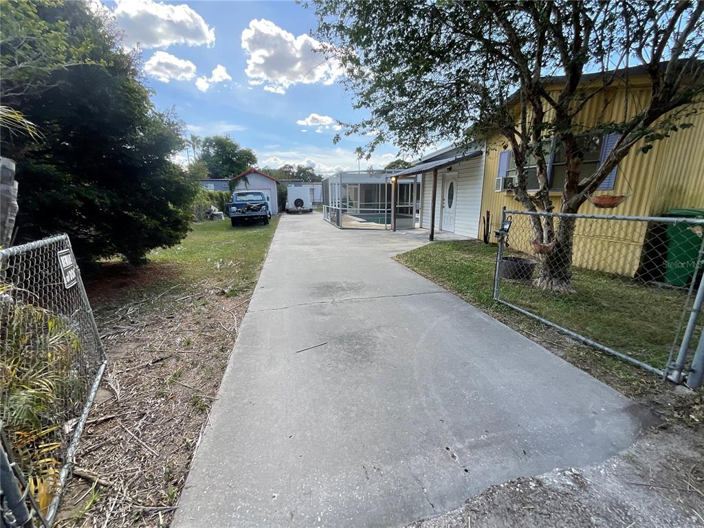 A concrete driveway leads toward a yellow house with a screened-in pool area — 700 JERSEY COURT, DUNDEE, FL