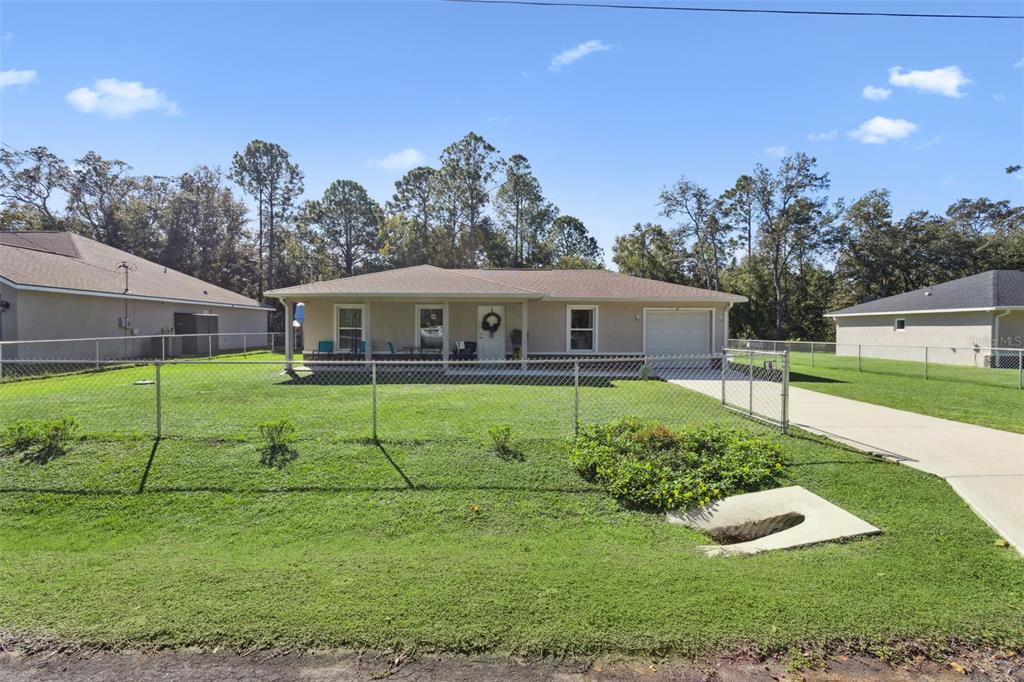 A single-story house with a beige exterior, a front porch, and a chain-link fence — 61 GUAVA TRAIL, OCKLAWAHA, FL