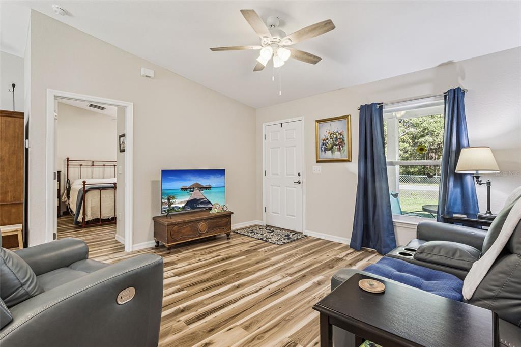 A living room features wood-look flooring, a ceiling fan, a television, and an entryway door — 61 GUAVA TRAIL, OCKLAWAHA, FL