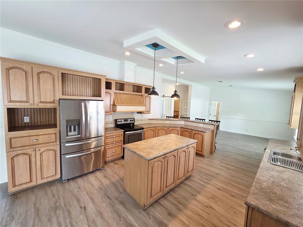 A kitchen features light wood cabinets, a central island, stainless steel appliances, and pendant lighting — 6607 IVY MIST LANE, DAVENPORT, FL