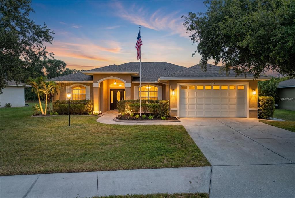 A single-story house with a two-car garage, a front lawn, and an American flag — 9110 64TH COURT E, PARRISH, FL