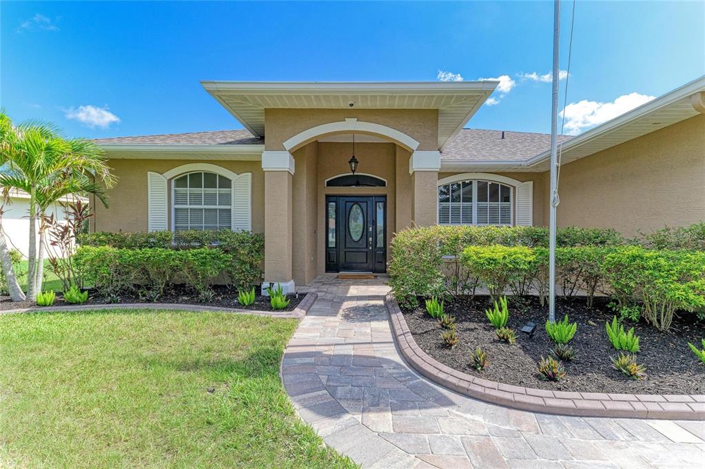 A tan house exterior features a paved walkway leading to a dark front door — 9110 64TH COURT E, PARRISH, FL