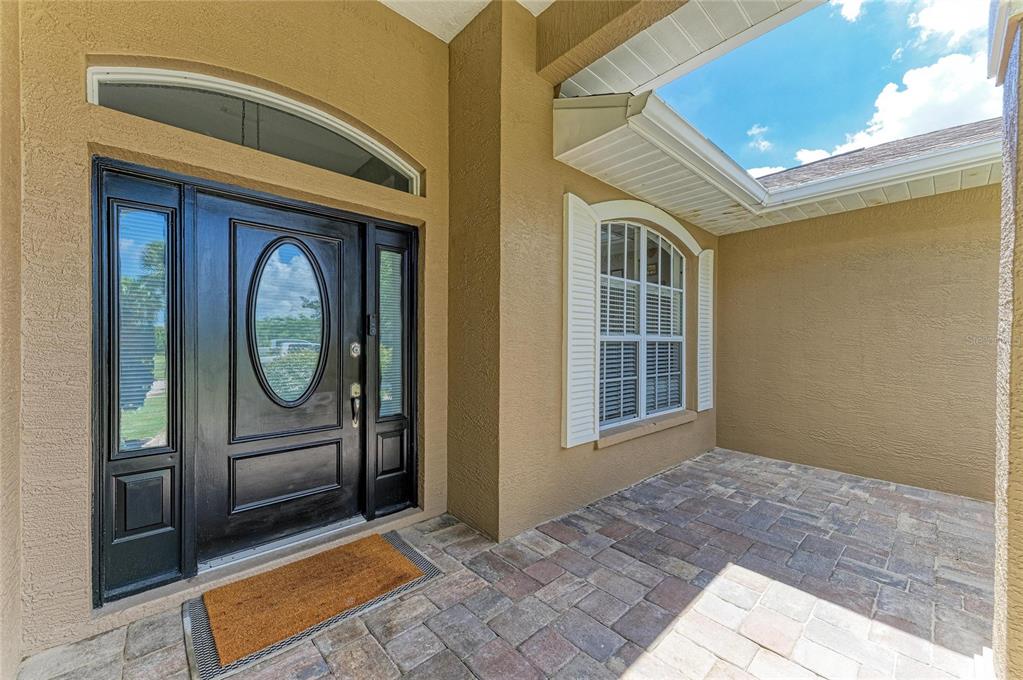 A covered entryway features a black front door, a window with shutters, and paved flooring — 9110 64TH COURT E, PARRISH, FL