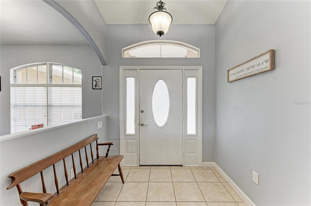 An entryway features a wooden bench, tile flooring, a white front door, and a light fixture — 9110 64TH COURT E, PARRISH, FL