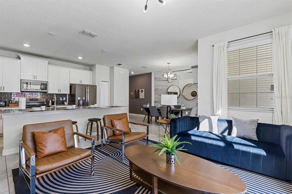An open-concept living room and kitchen featuring a blue sofa, leather chairs, and white cabinetry — 8990 STINGER DRIVE, CHAMPIONS GATE, FL