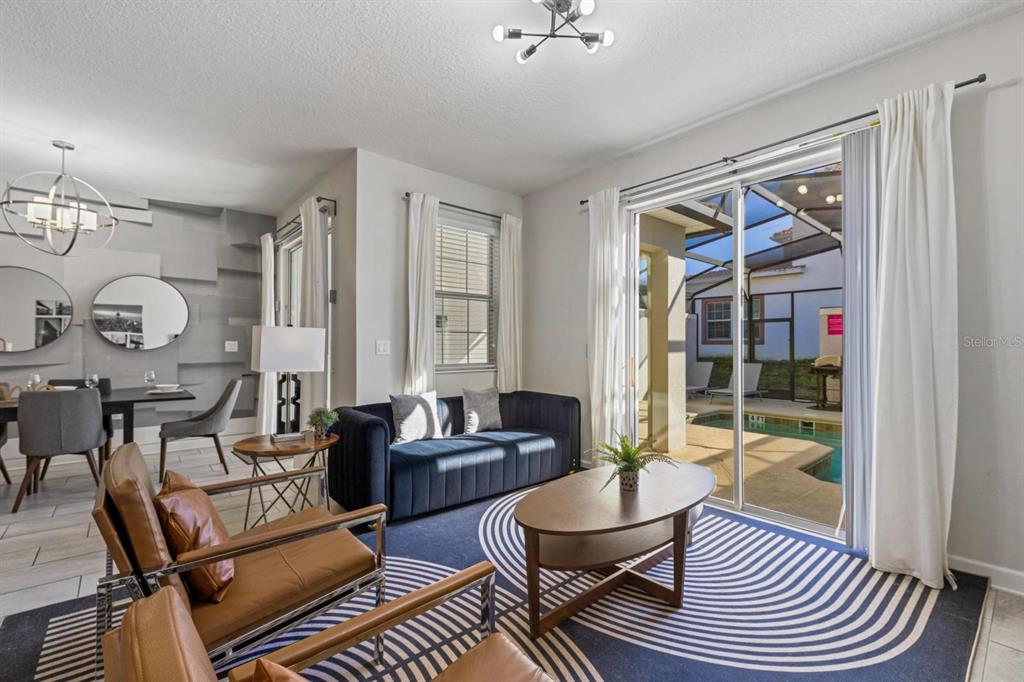 A living room with a blue sofa, leather chairs, and a sliding door to a pool — 8990 STINGER DRIVE, CHAMPIONS GATE, FL