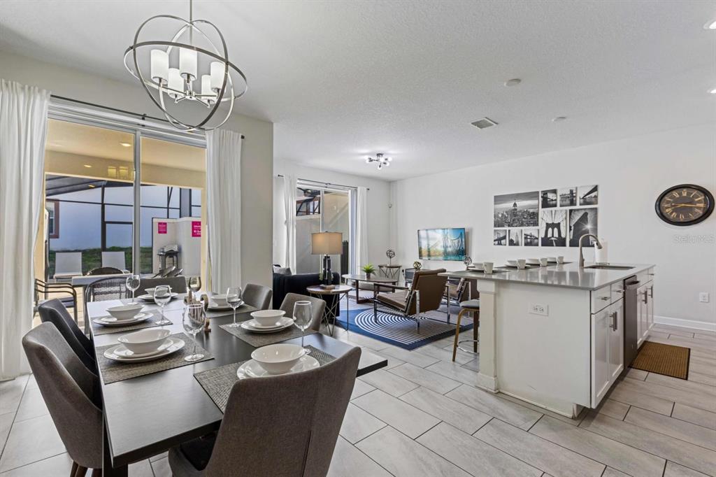 An open-concept dining and living area features a kitchen island, tile flooring, and sliding doors — 8990 STINGER DRIVE, CHAMPIONS GATE, FL