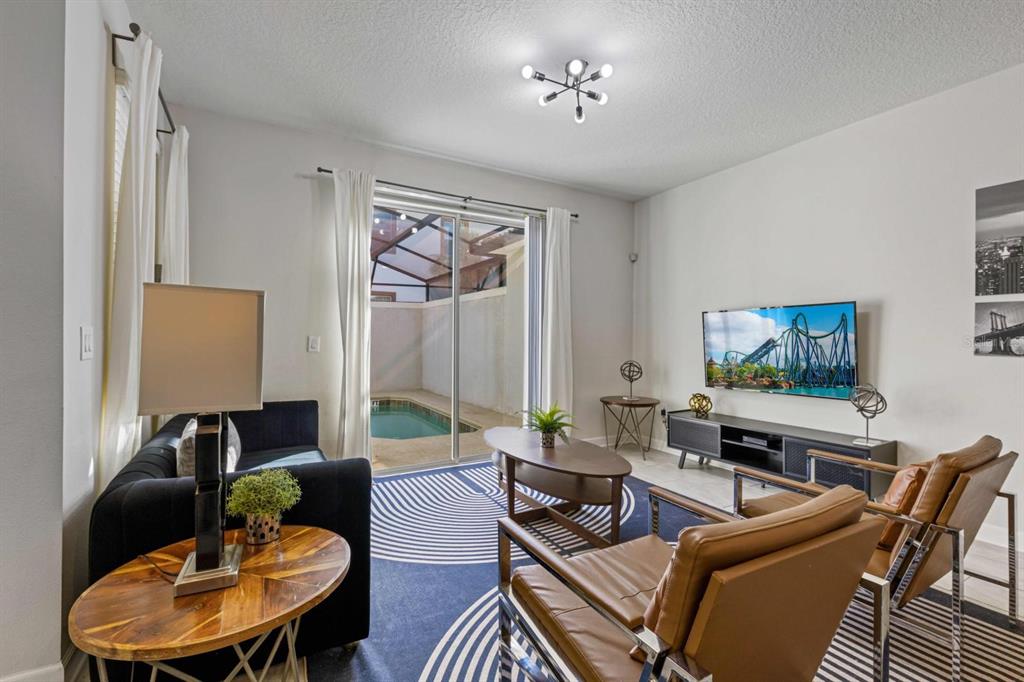 A living room with a dark sofa, two leather chairs, and a sliding door to a pool — 8990 STINGER DRIVE, CHAMPIONS GATE, FL