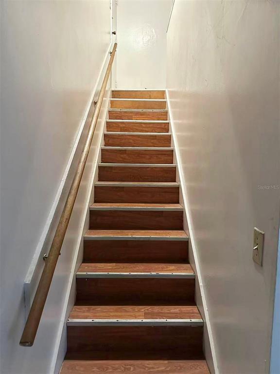 A straight wooden staircase with a single handrail ascends between two plain white walls — 914 SW 8TH AVENUE UNIT 42, GAINESVILLE, FL