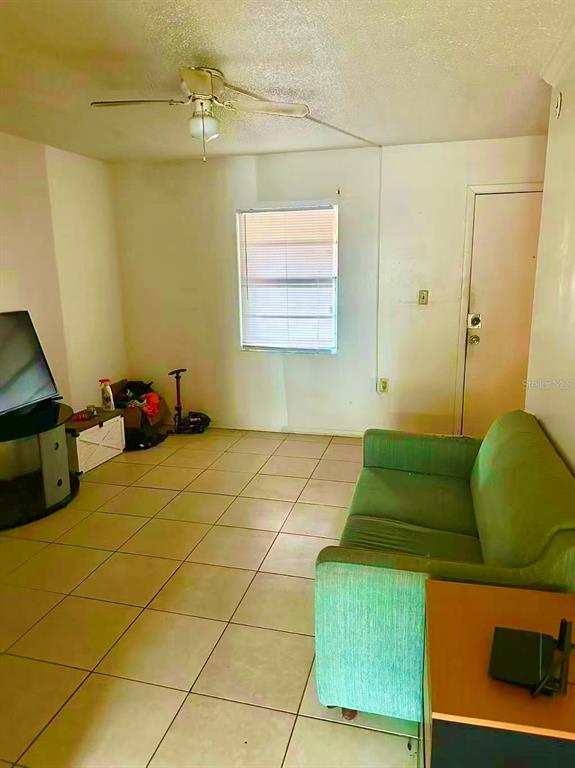 A living room features a green sofa, tiled floors, a ceiling fan, and a window — 914 SW 8TH AVENUE UNIT 42, GAINESVILLE, FL